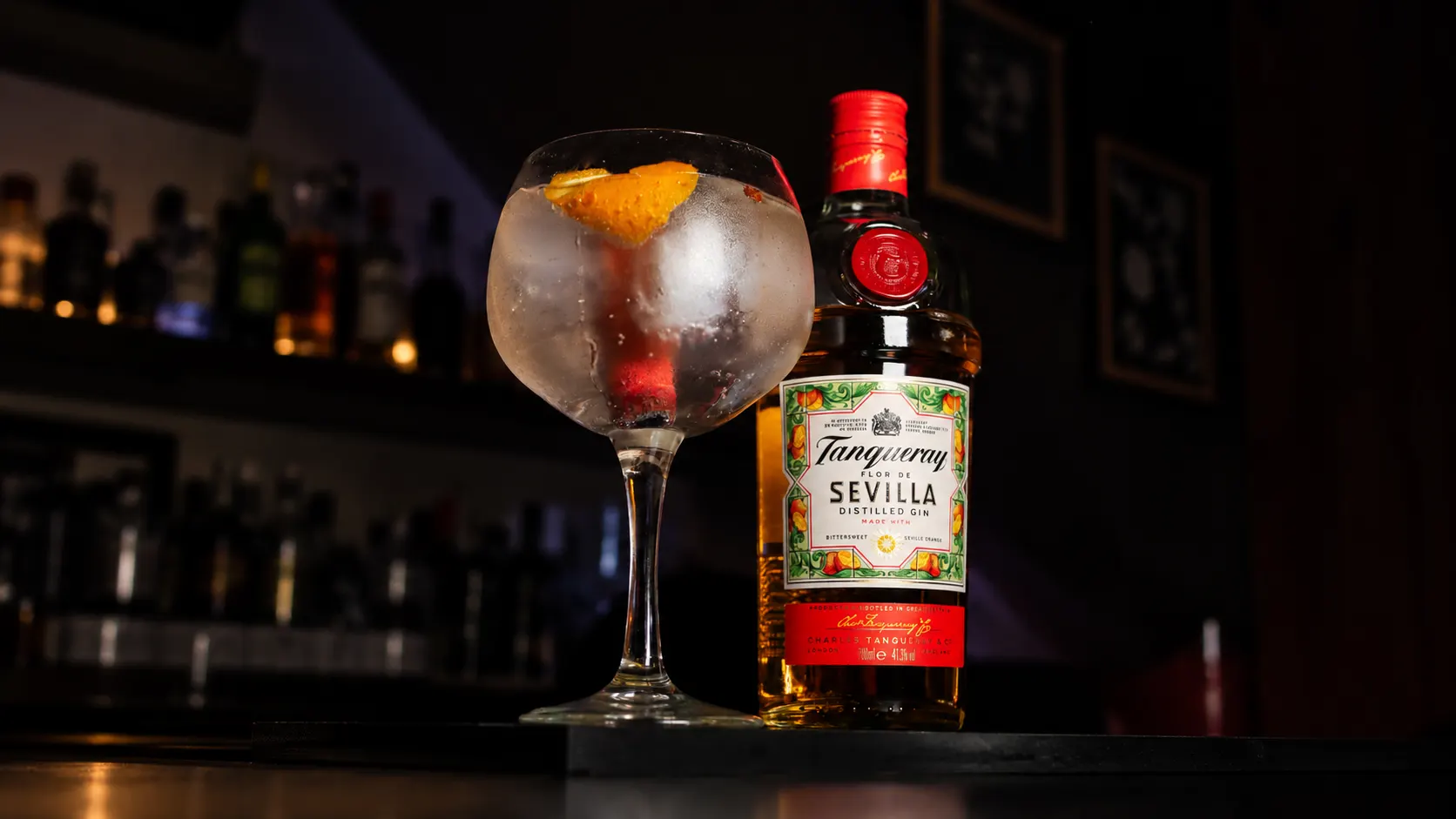 Um gin tónico com casca de laranja num copo balão, ao lado de uma garrafa de Tanqueray Sevilla.