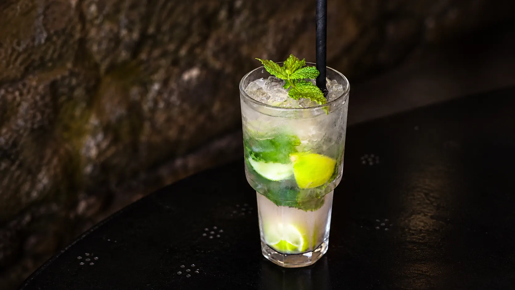 Um mojito num copo alto, com gelo picado, lima e um raminho de hortelã.